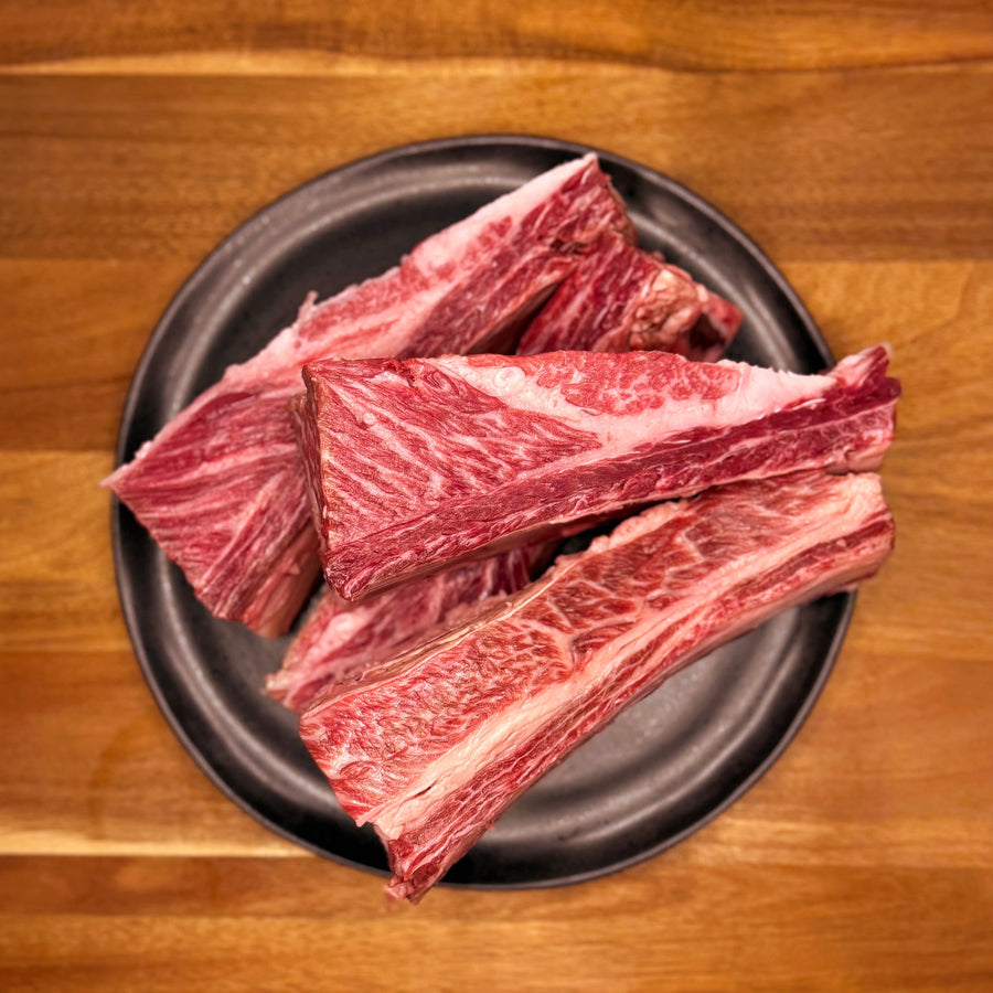 Raw beef wagyu dino ribs on a dark plate on a wooden table